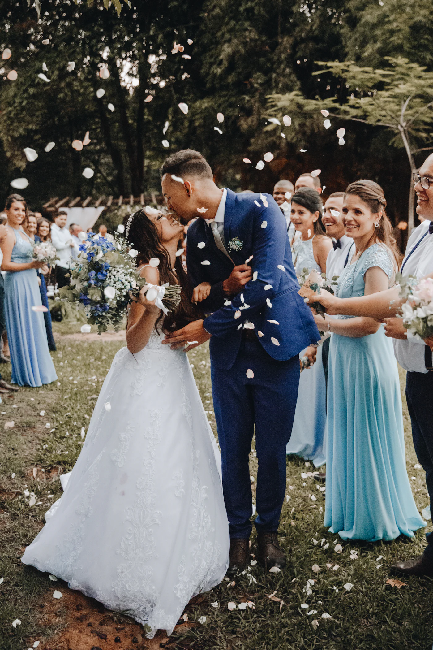 Newlyweds kissing as joyful wedding guests shower them with flower petals at an outdoor celebration